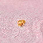 Close up of a floral inspired 18K gold nose pin placed on a soft pink textured background highlighting its intricate design