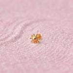 Close up of a floral design 18K gold nose pin placed on a soft pink textured background highlighting fine detailing
