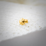 Gold floral nose pin photographed on a textured white surface showing its intricate detailing