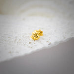 Close up of a gold nose pin placed on a textured white stone surface highlighting its smooth polish and compact design