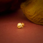 Close up of a gold nose pin placed on a warm textured surface highlighting its polished finish and intricate detailing