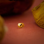 Close up of a small floral gold nose pin placed on a warm terracotta surface highlighting its intricate carved detailing