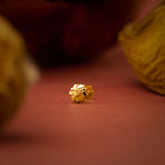 Close up of a small gold nose pin placed on a warm textured surface highlighting its polished finish