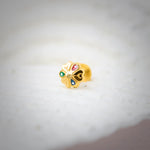 Close-up of multicolour stone 18K nose pin gold placed on a soft white surface highlighting its vibrant detailing