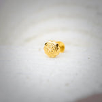 Close-up of an intricately carved 18K nose pin gold placed on a soft white surface highlighting its detailed floral design