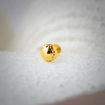 Glossy round 18K nose pin gold placed on a textured white surface highlighting its smooth polished finish