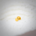 Close up view of a plain round 18K gold nose pin placed on a white textured surface showing a smooth polished finish