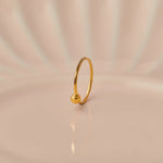 Close up of minimalist 18K gold nose ring with a small ball accent standing upright on a soft beige background with subtle light reflections