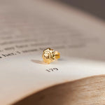 Gold textured flower stud earring, close-up on paper