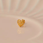 Gold heart-shaped nose stud with filigree scrollwork and twisted border on beige background