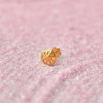 Gold round medallion nose stud with cutout flower pattern on pink glitter background
