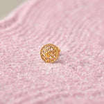 Close up of a textured round 18K gold nose pin placed on a soft pink background highlighting fine detailing