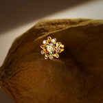 A gold star-shaped stud earring with a textured center bead and multicolor stones set along the star points, placed on a textured brown fabric background