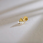 Product shot of a gold nose stud with a solid gold triangle above three gemstones
