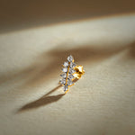 Nose pin gold with vertical leaf cluster design featuring multiple sparkling stones set in a polished gold base on a soft neutral background