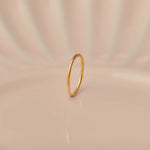 Front view of slim plain 18K gold hoop nose ring standing upright on a soft beige background with subtle light reflections