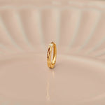 Side view of minimalist 18K gold hoop nose ring standing upright on a soft beige background with subtle light reflections