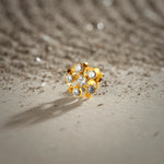 An 18K gold nose pin shaped like a flower with swirling gold loops, a small star-shaped center, and clear crystal petals, photographed on a light textured surface