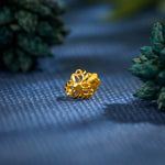 Close up of an intricate floral gold nose pin placed on a textured blue surface with greenery in the background highlighting its ornate design