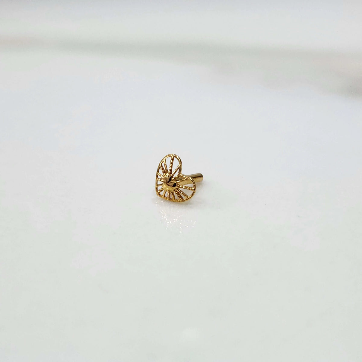 Front view of a tiny 18K nose pin gold placed on a white background showing its small size and fine detailing