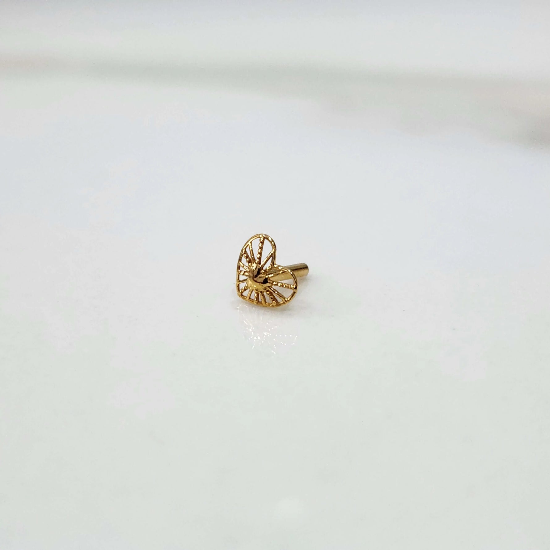 Front view of a tiny 18K nose pin gold placed on a white background showing its small size and fine detailing