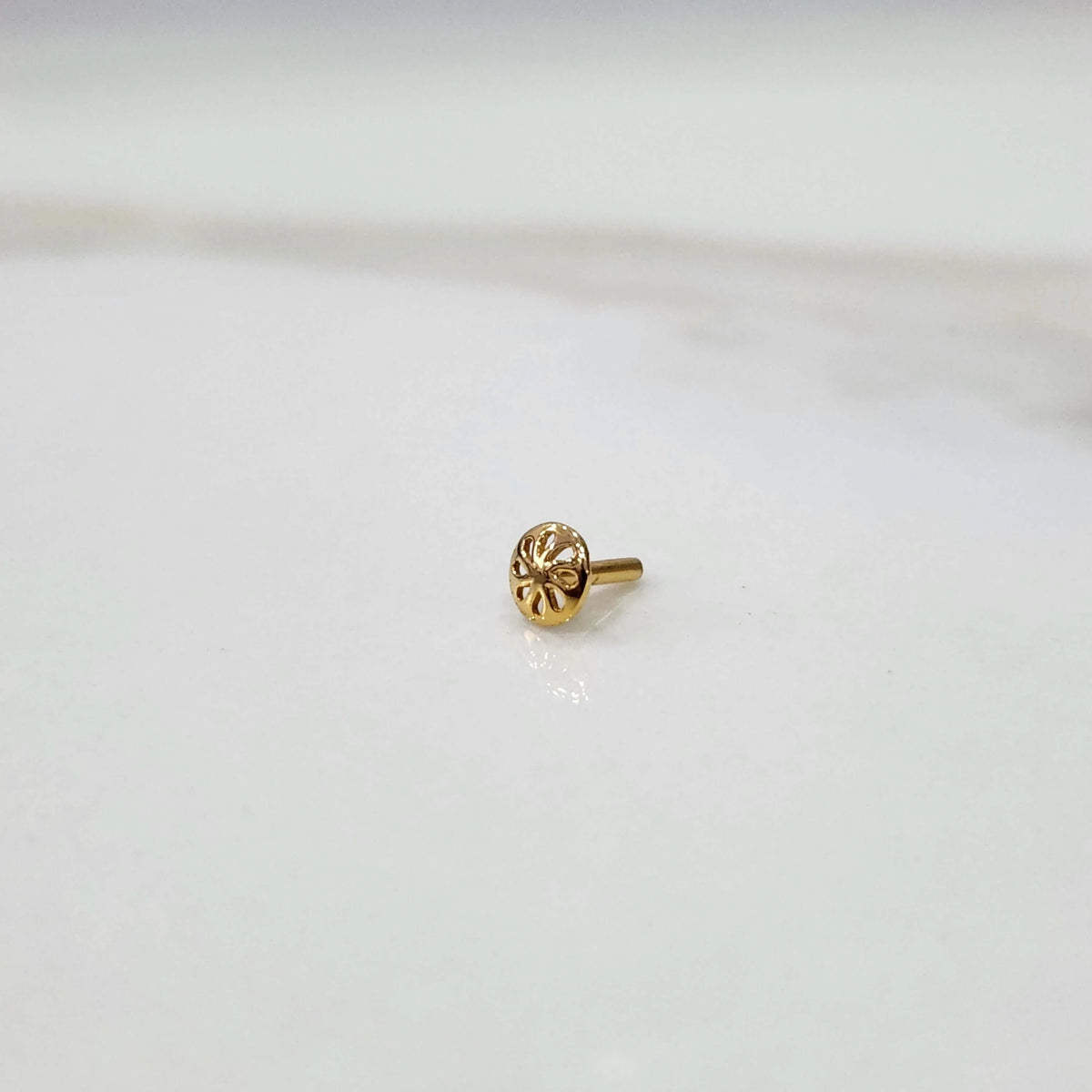 Side view of a tiny gold nose pin on a white surface highlighting its lightweight structure and polished finish