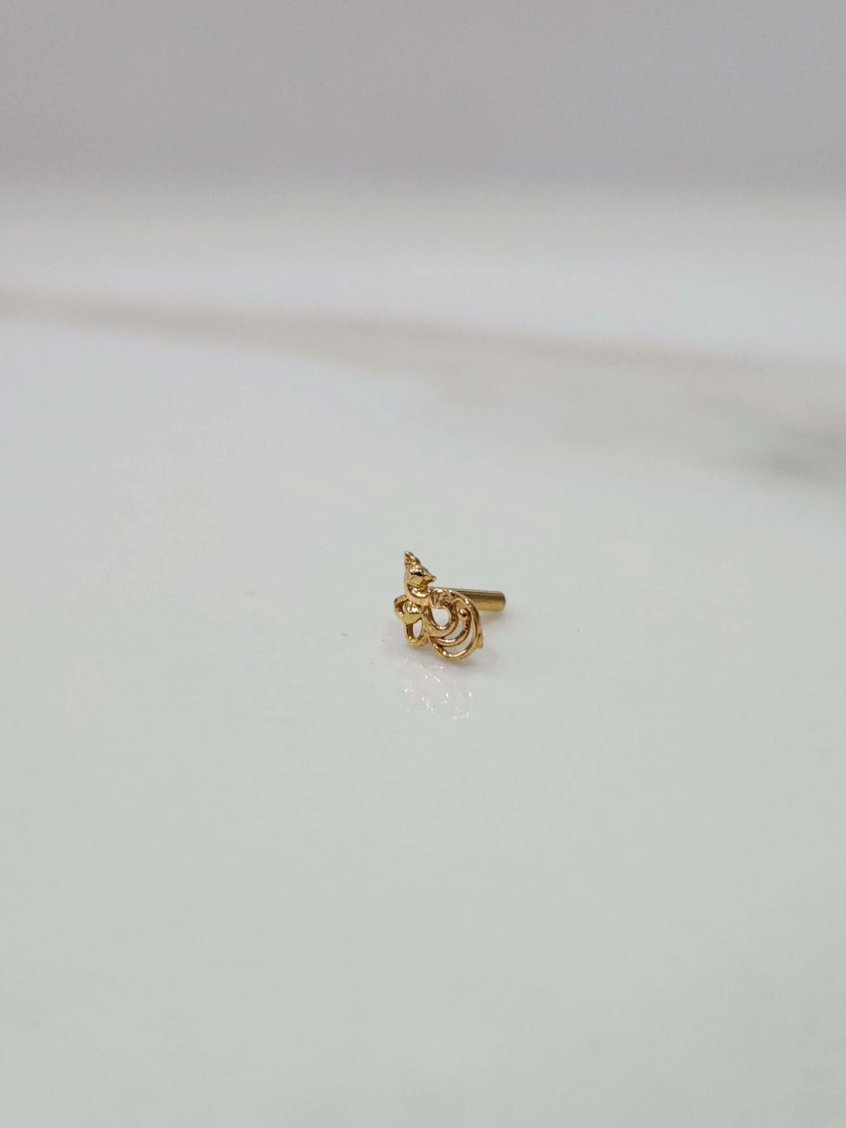 Front view close up of a small 18K nose pin gold placed on a white surface showing compact size and fine detailing