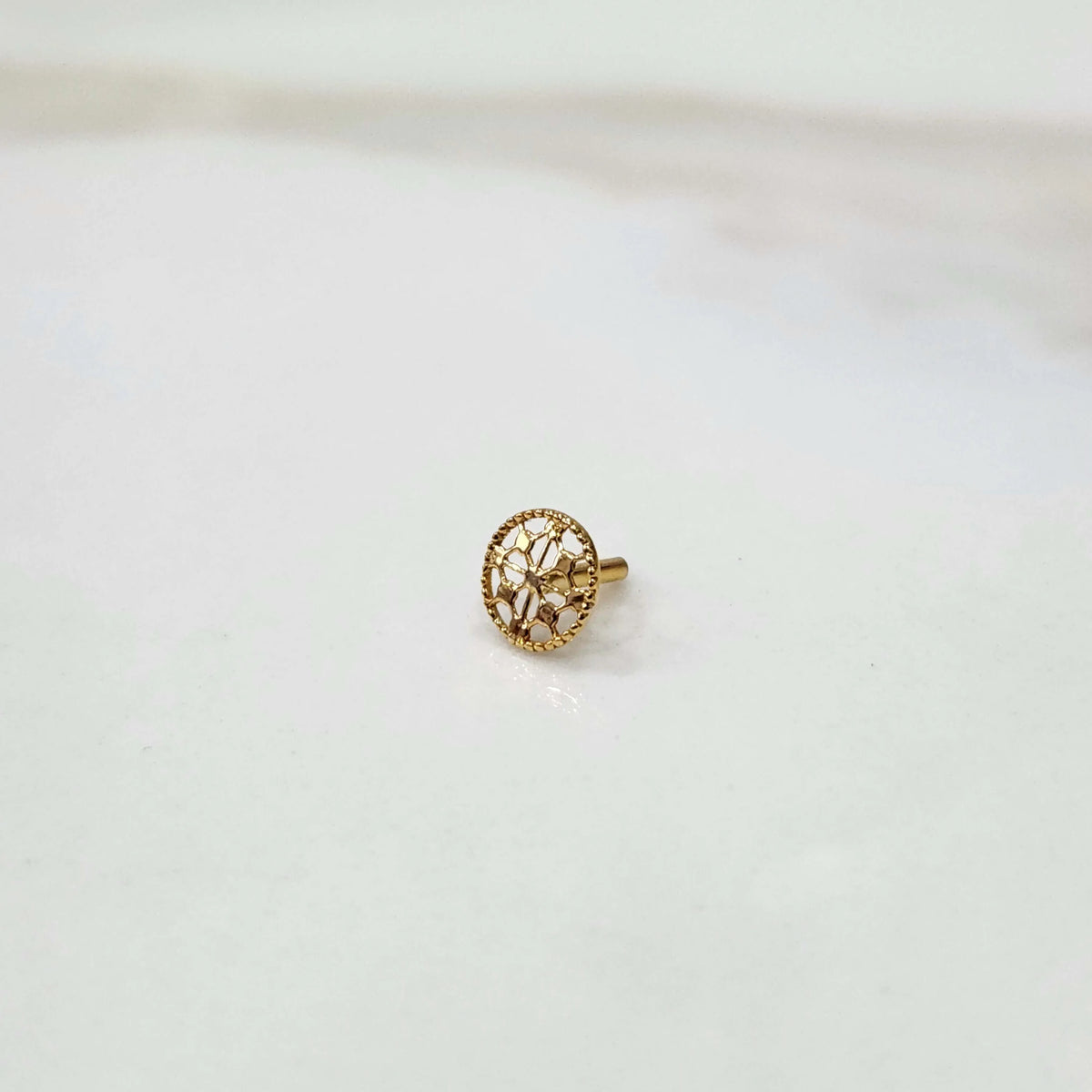 Front view of a small round 18K gold nose pin placed on a white background showcasing fine detailing and compact size