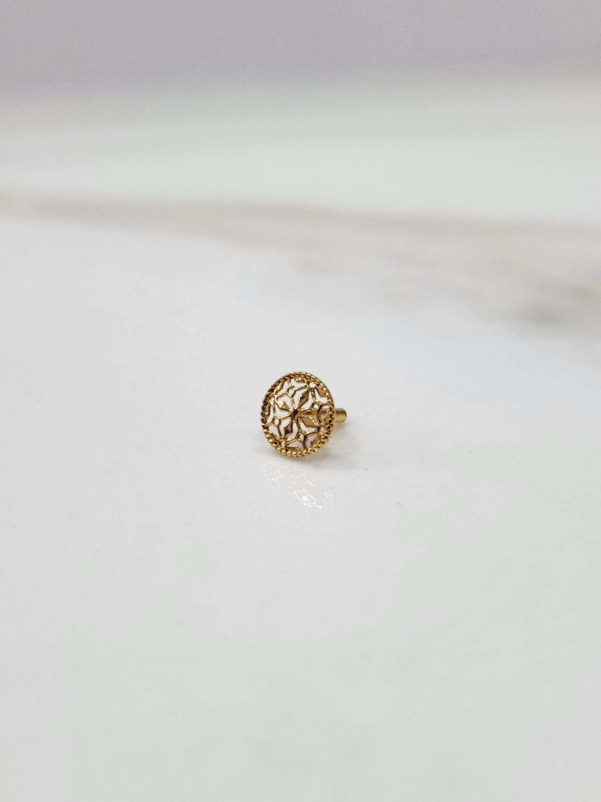 Side view of a delicate 18K nose pin gold on a light background showing its fine finish and minimal design