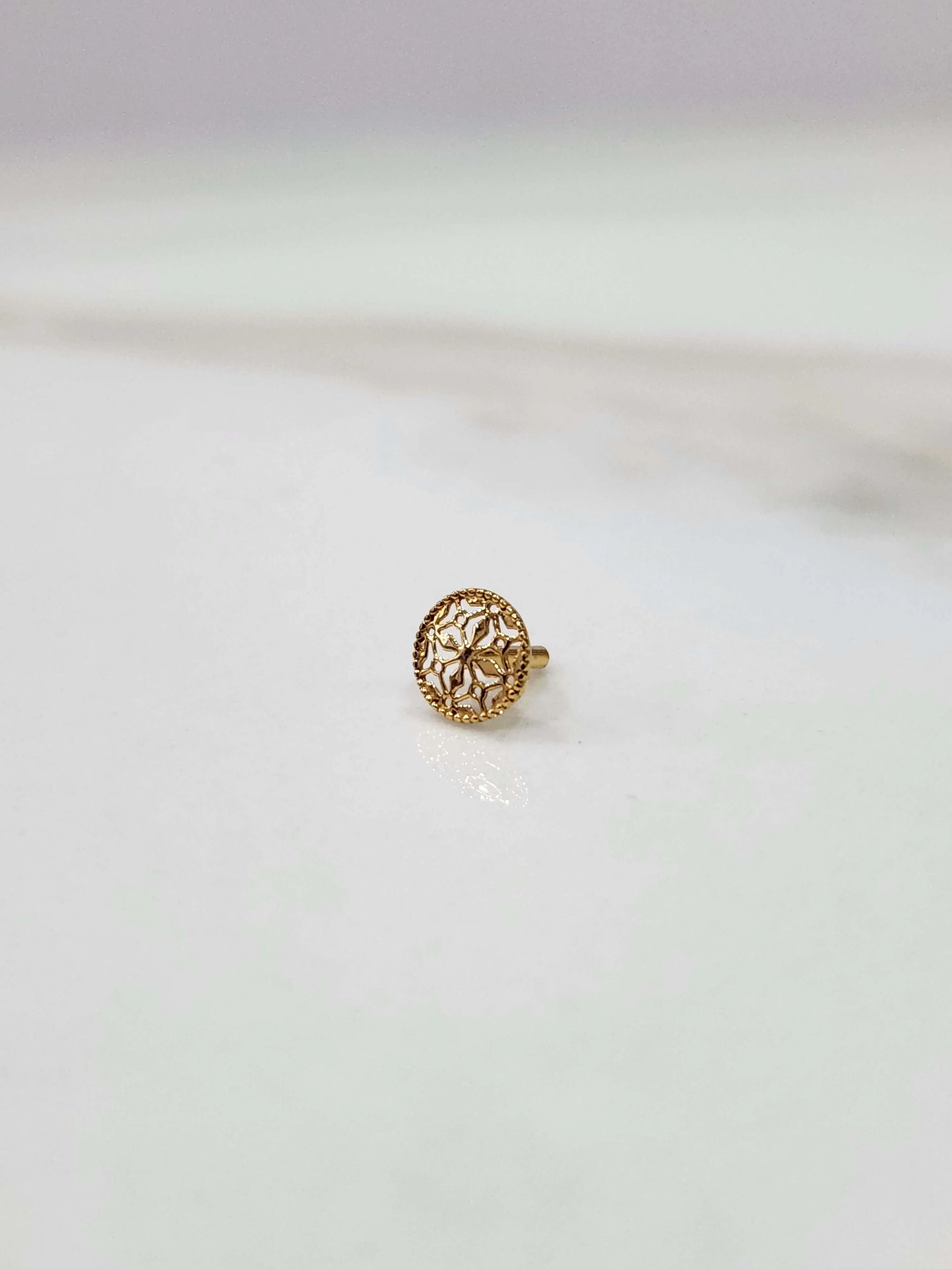 Side view of a delicate 18K nose pin gold on a light background showing its fine finish and minimal design