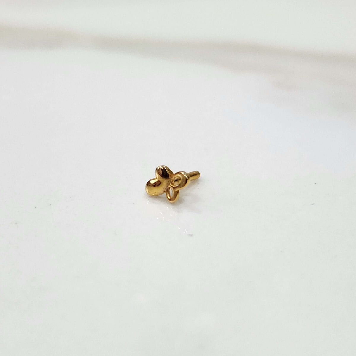 Close up of a small floral 18K nose pin gold placed on a clean white surface highlighting its delicate handcrafted detailing