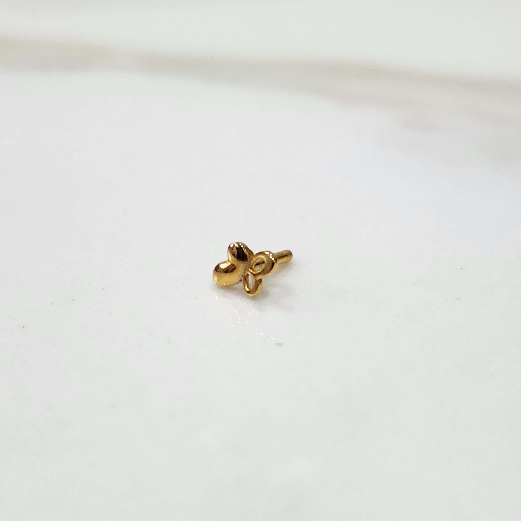 Close up of a small floral 18K nose pin gold placed on a clean white surface highlighting its delicate handcrafted detailing