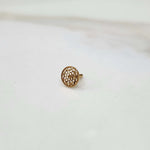 Front view of a small round 18K nose pin gold placed on a white surface highlighting its detailed texture

