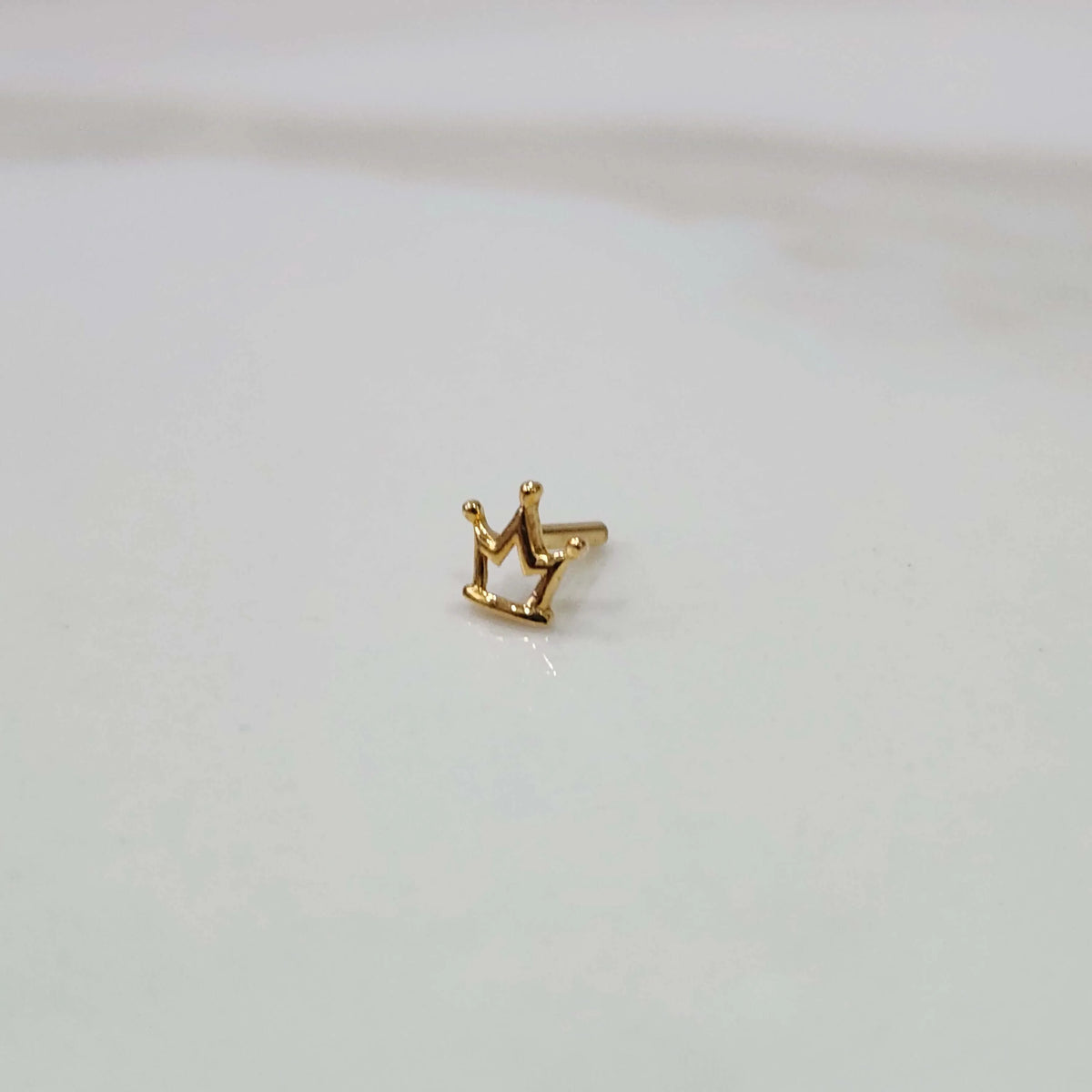 Side view of a small crown motif gold nose pin placed on a white surface showing its compact size and finish