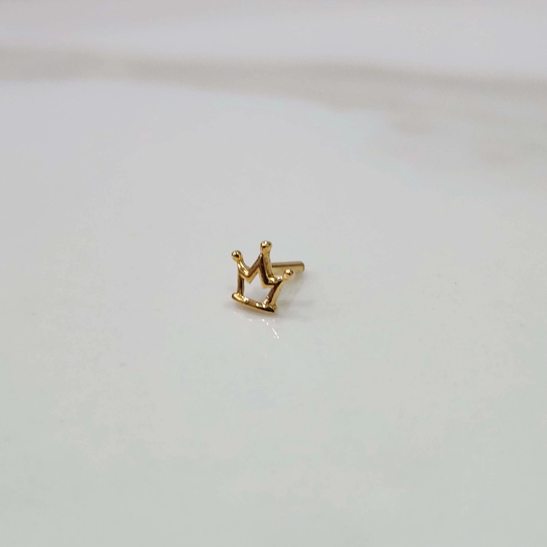 Side view of a small crown motif gold nose pin placed on a white surface showing its compact size and finish