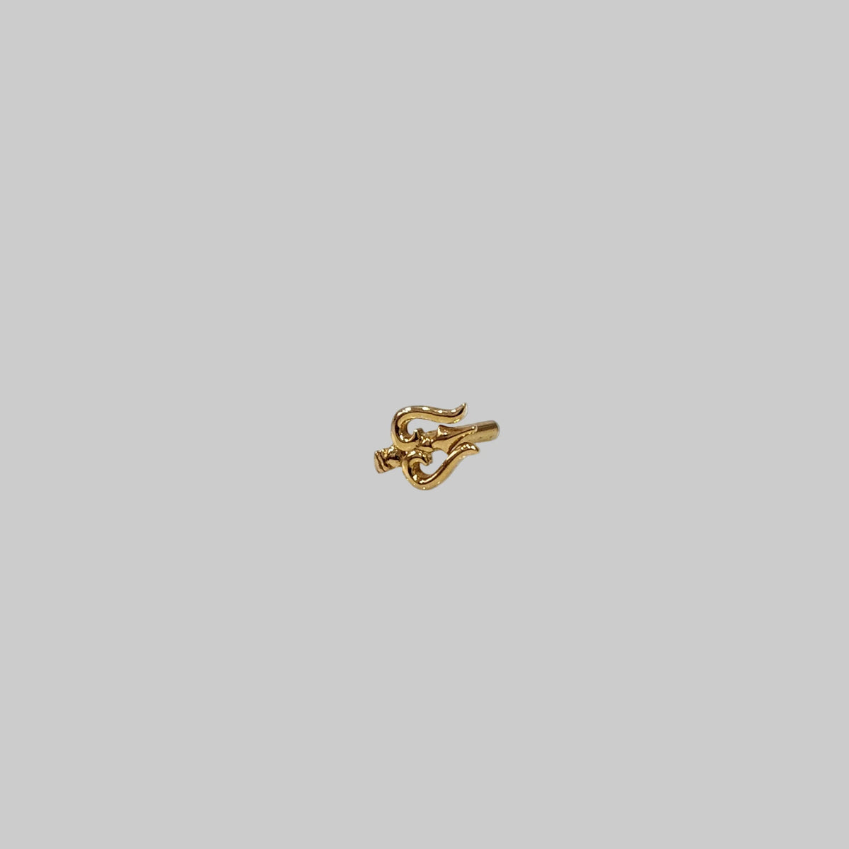 Small gold nose pin placed on grey surface highlighting delicate craftsmanship