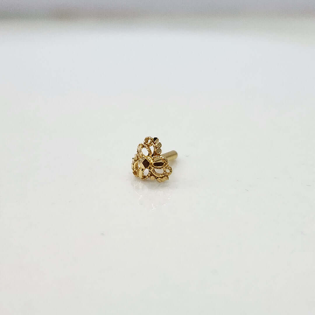 Side angle view of the floral gold nose pin on a white surface highlighting its depth and polished finish