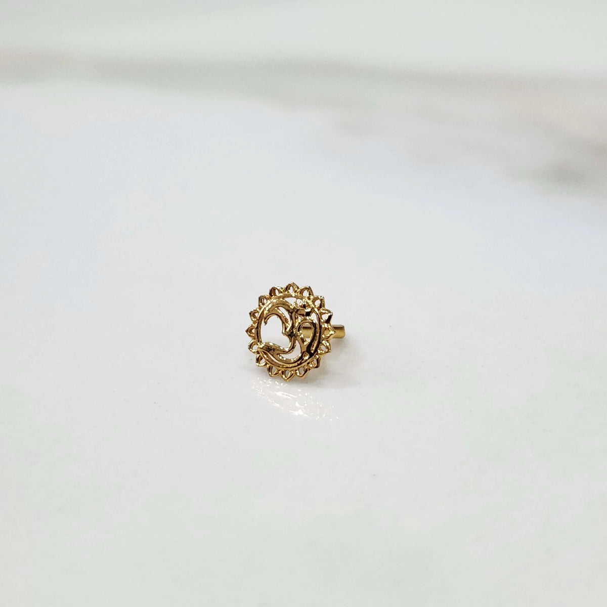 Close-up of a delicate 18K nose pin gold placed on a white surface showing fine craftsmanship and polished finish