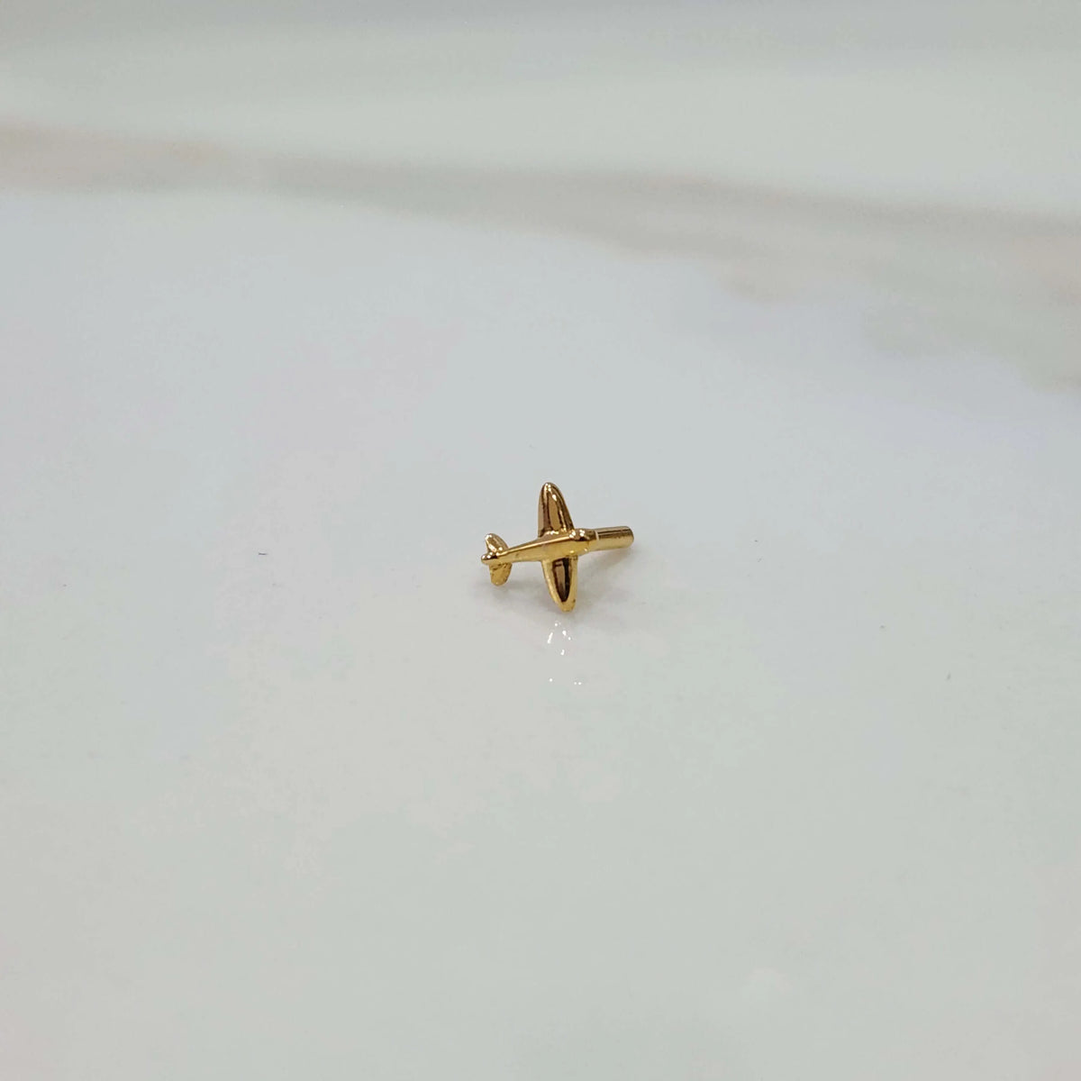 Side view of a small 18K gold nose pin placed on a white background showing its compact size and simple design