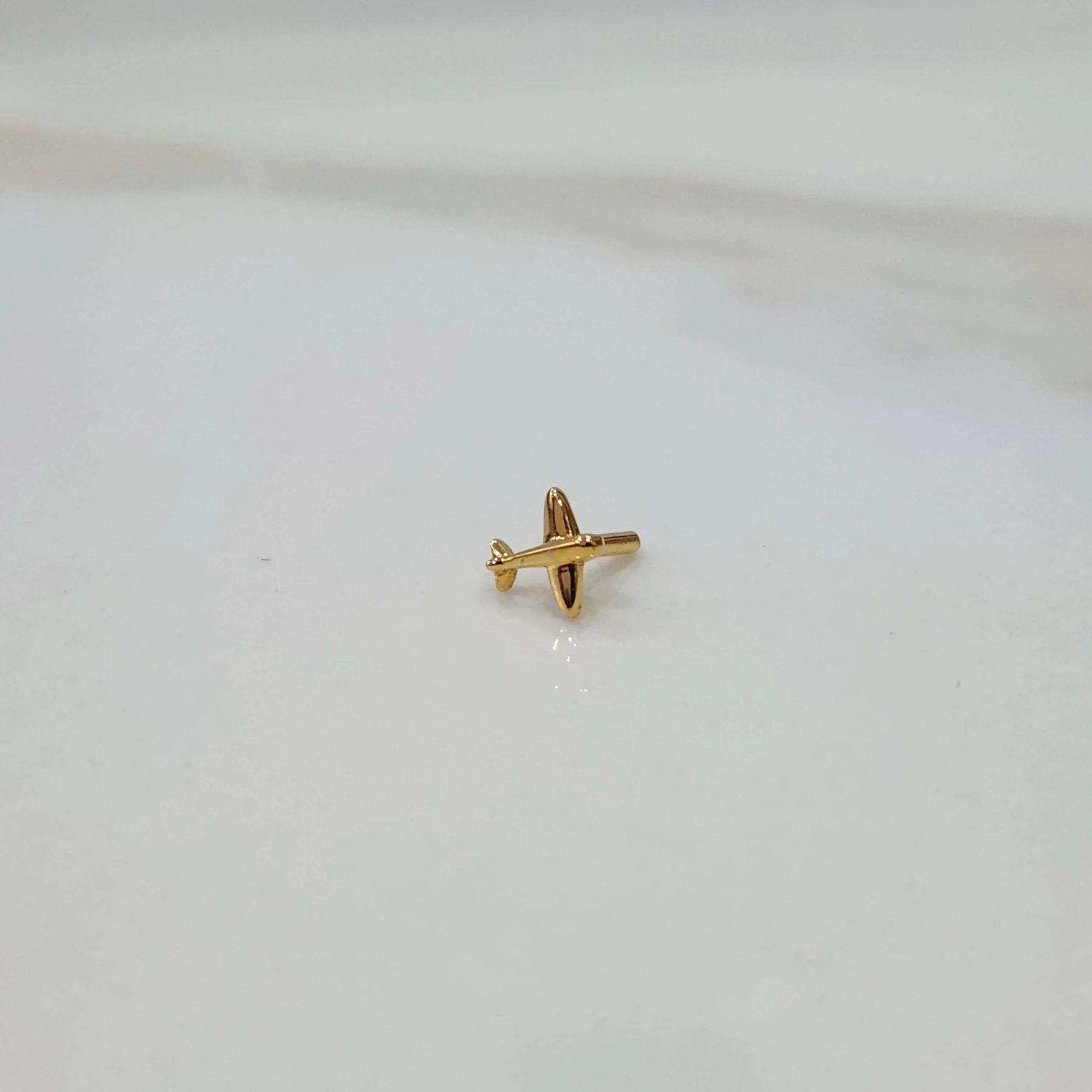Side view of a small 18K gold nose pin placed on a white background showing its compact size and simple design