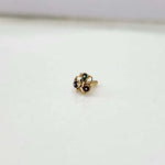Close up of small floral patterned 18K gold nose pin placed on a white surface highlighting its fine detailing