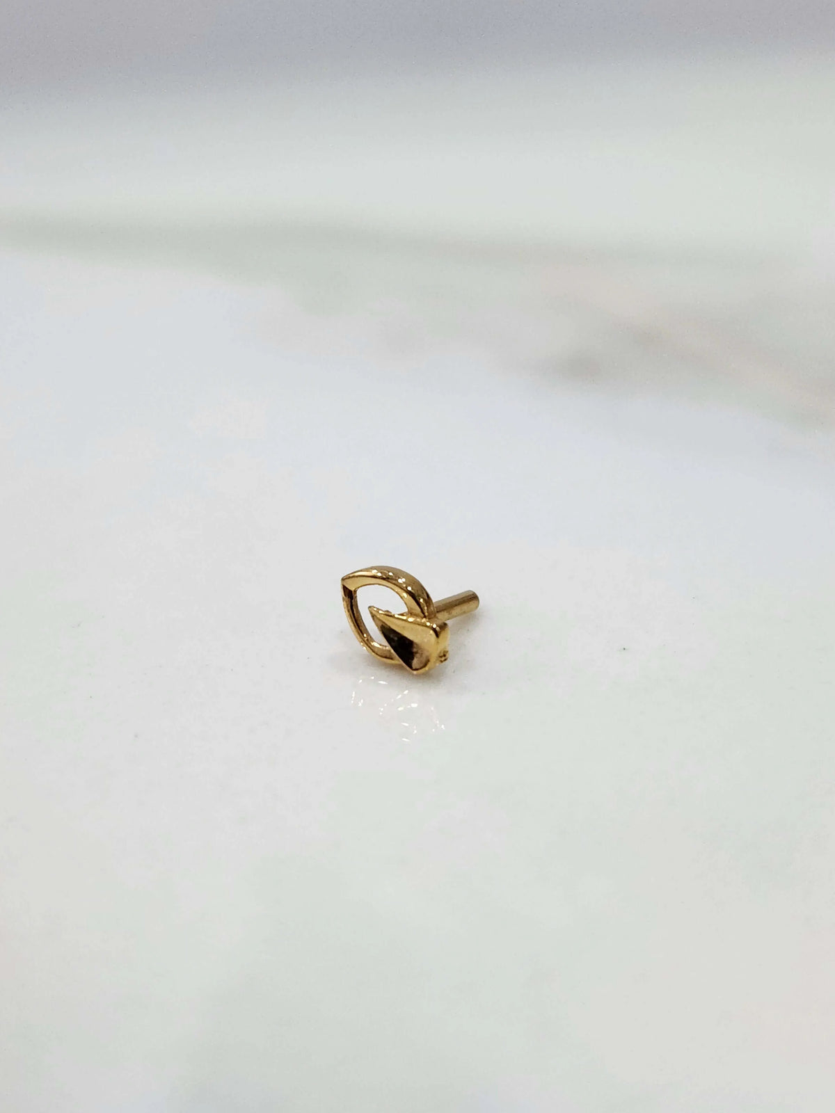 Side view of a tiny 18K gold nose pin on a white surface highlighting its compact lightweight design