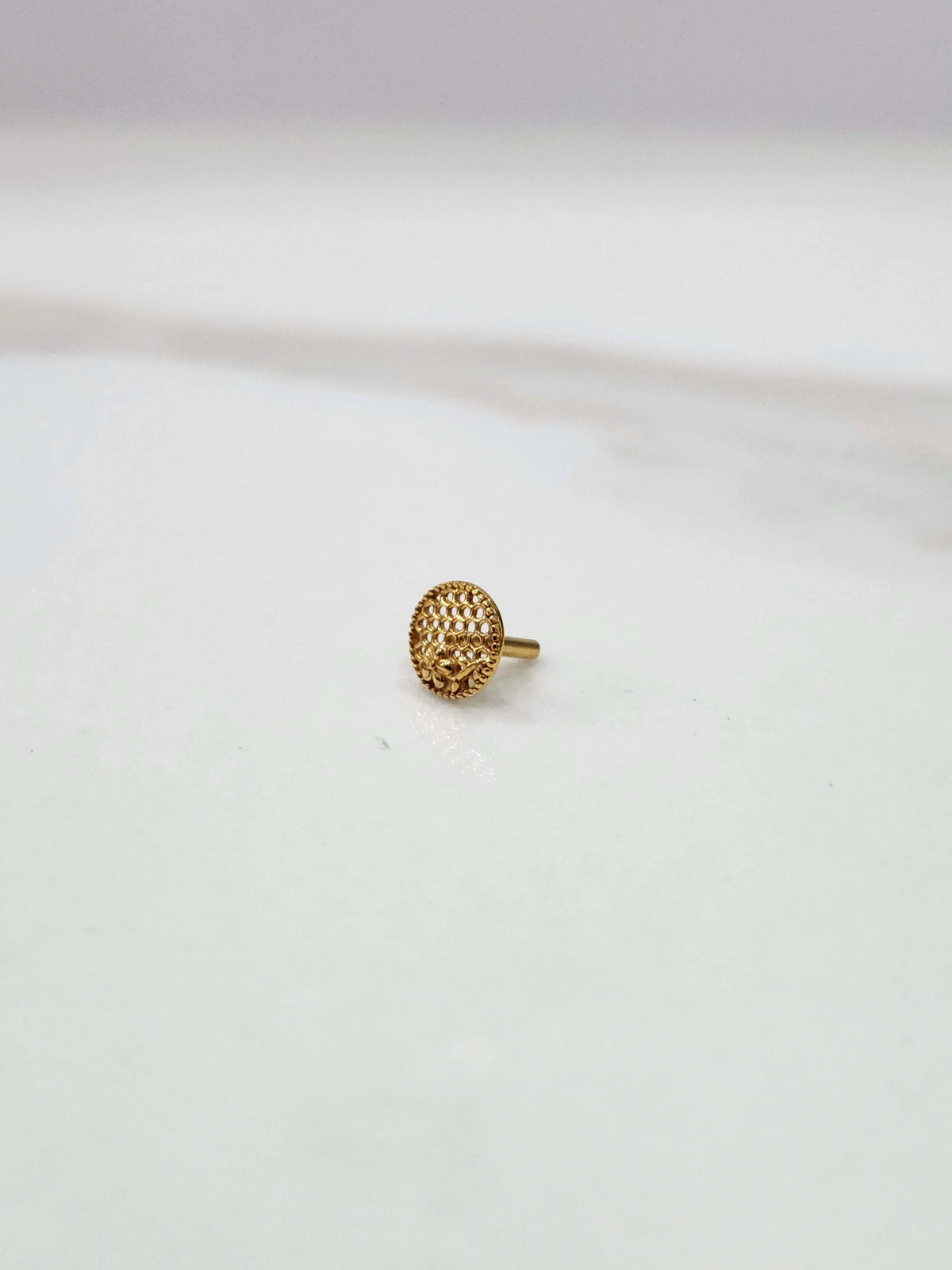 Side view of a small round 18K gold nose pin placed on a white surface showcasing its compact size and polished finish