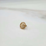 Front view of small textured 18K gold nose pin placed on a white surface highlighting its fine detailing