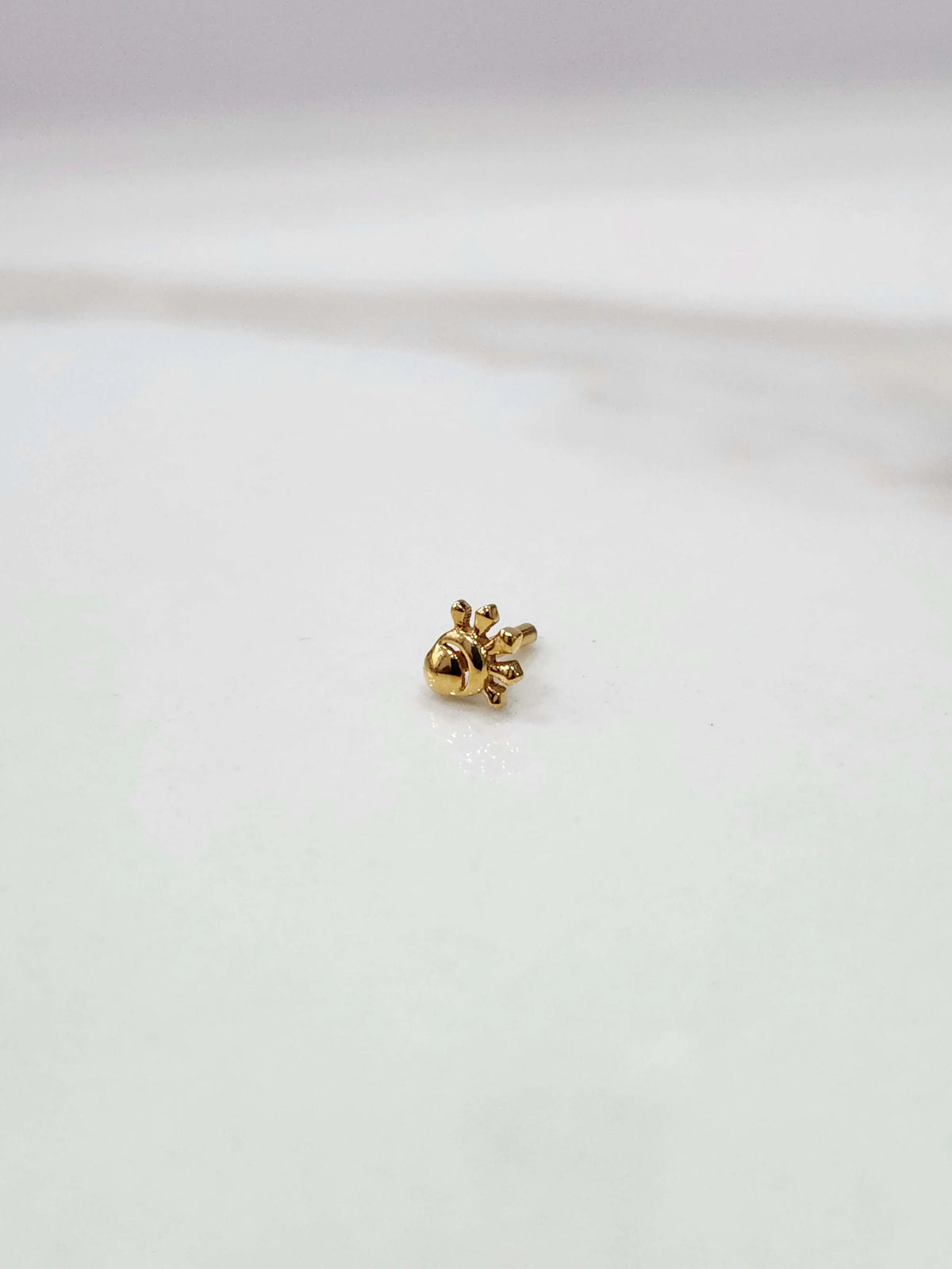 Side view of a delicate 18K nose pin gold placed on a white surface showcasing its fine finish and minimal detailing