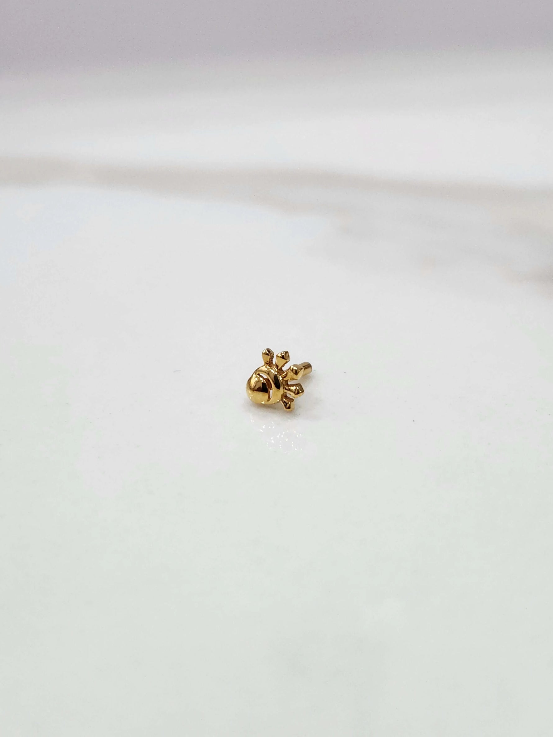 Side view of a delicate 18K nose pin gold placed on a white surface showcasing its fine finish and minimal detailing