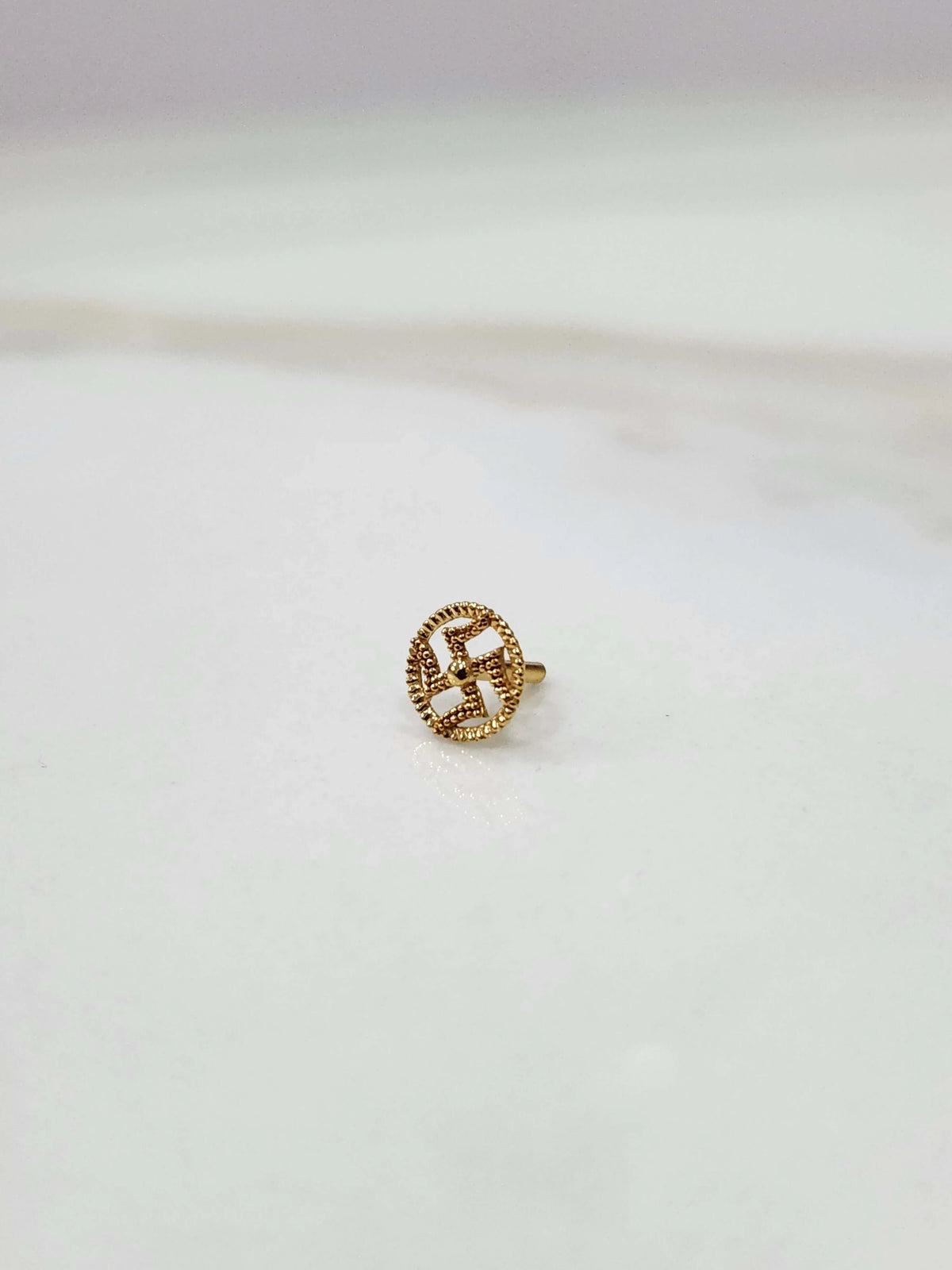 Close-up of a tiny 18K nose pin gold placed on a white surface showing fine detailing and compact finish