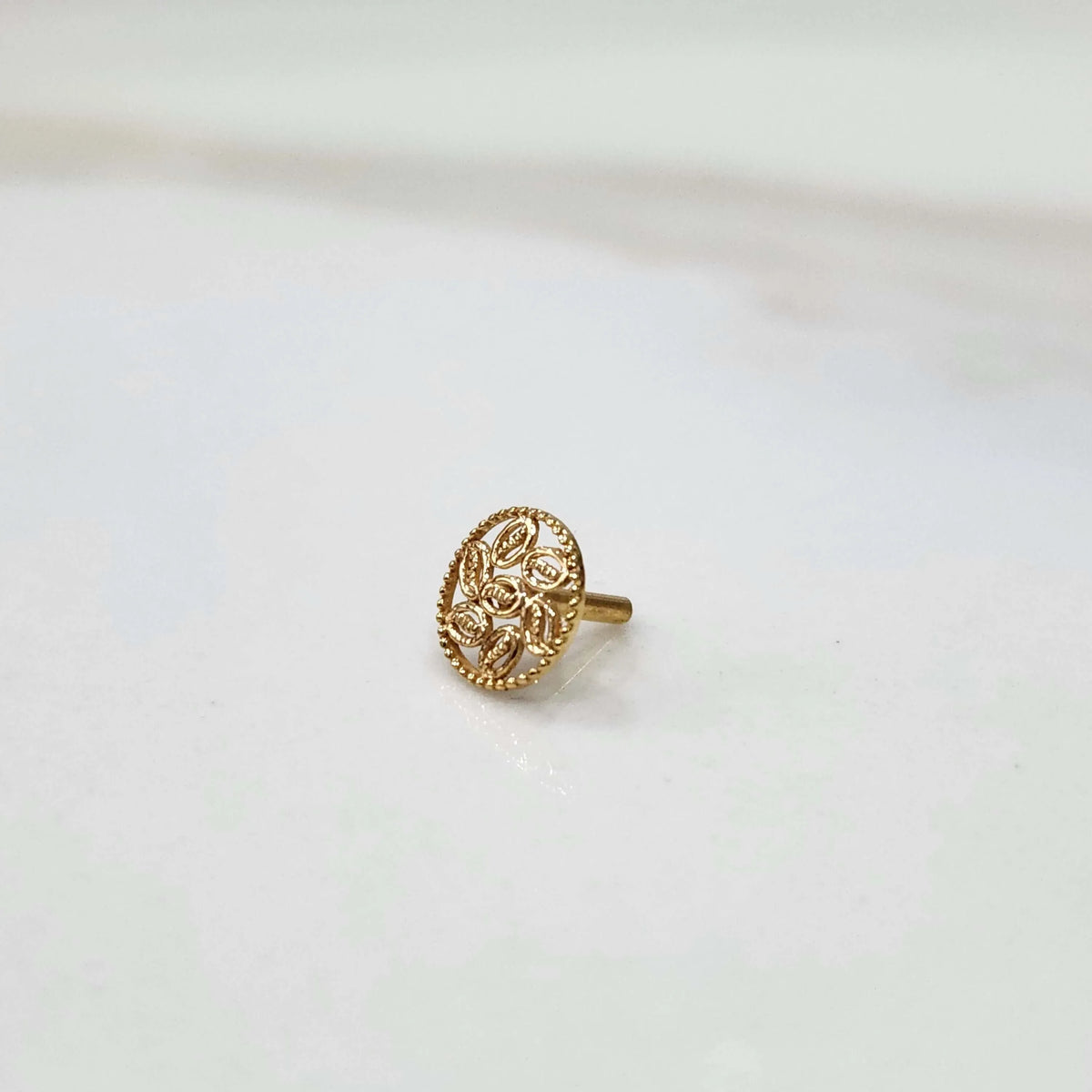 Side view of a delicate 18K gold round-pattern nose pin placed on a white surface highlighting its detailing