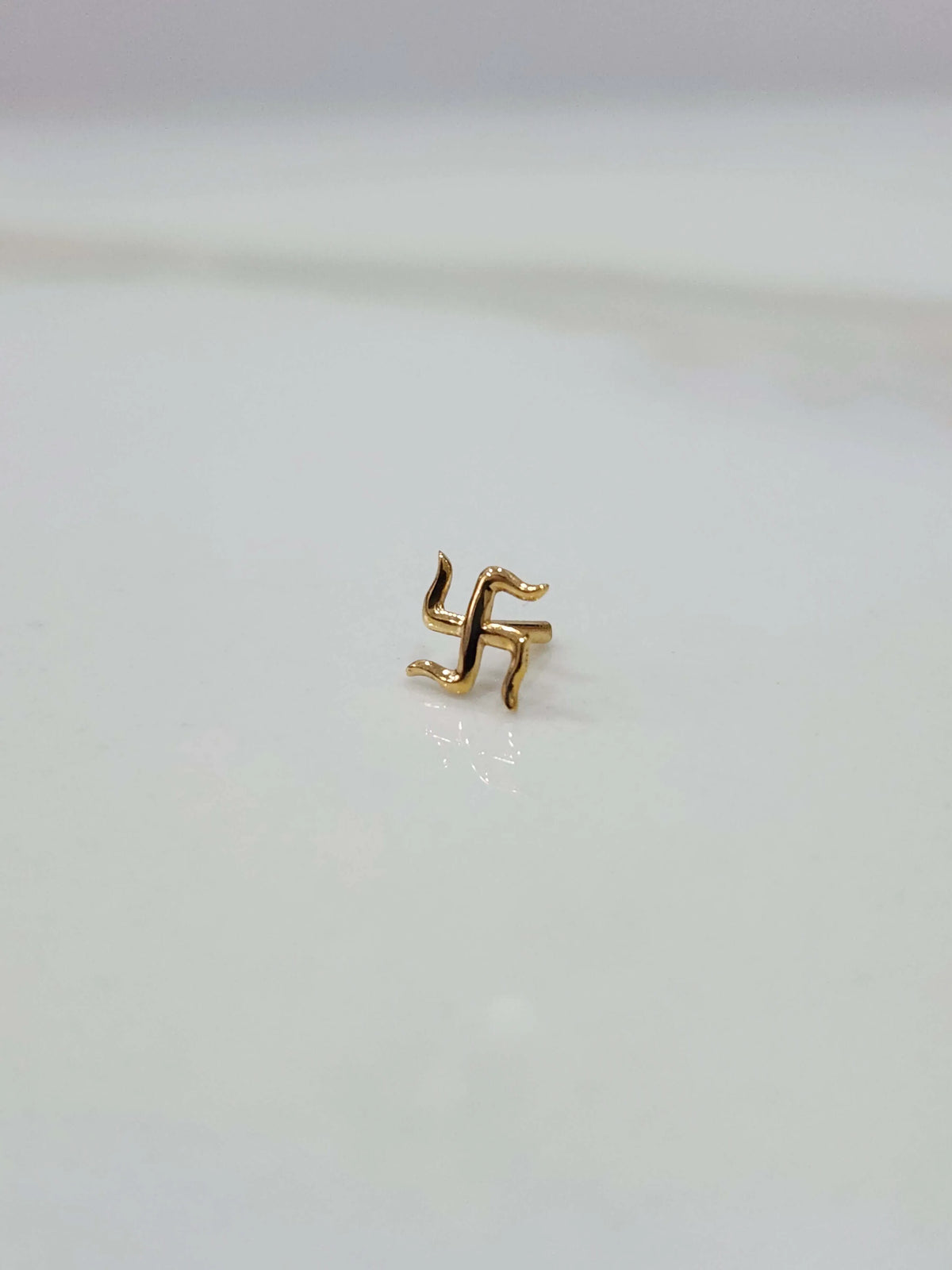 Close up of a small swastik 18K nose pin gold placed on a white surface showing fine detailing and compact size