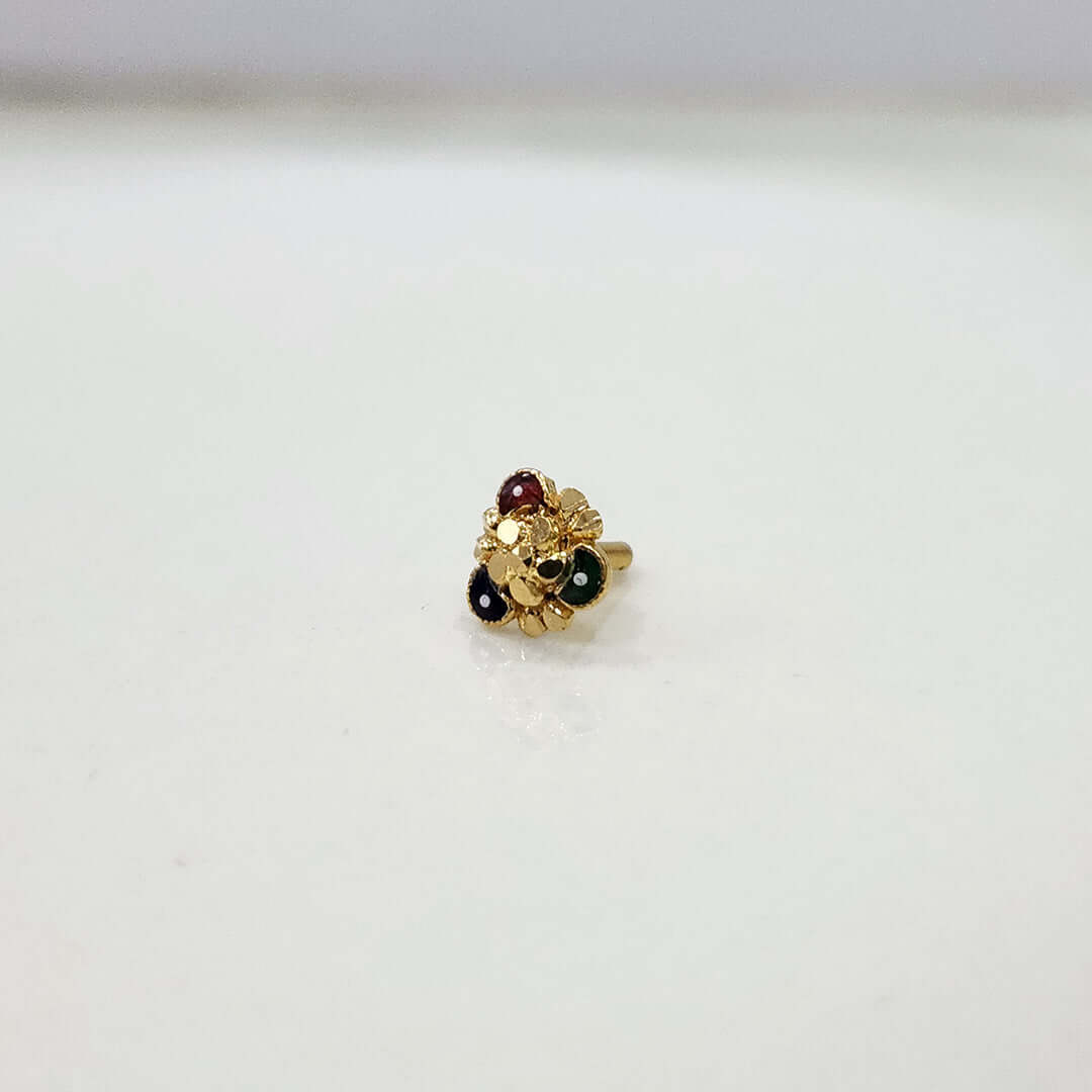Front view of floral gold nose pin with green and red stone detailing on a white surface